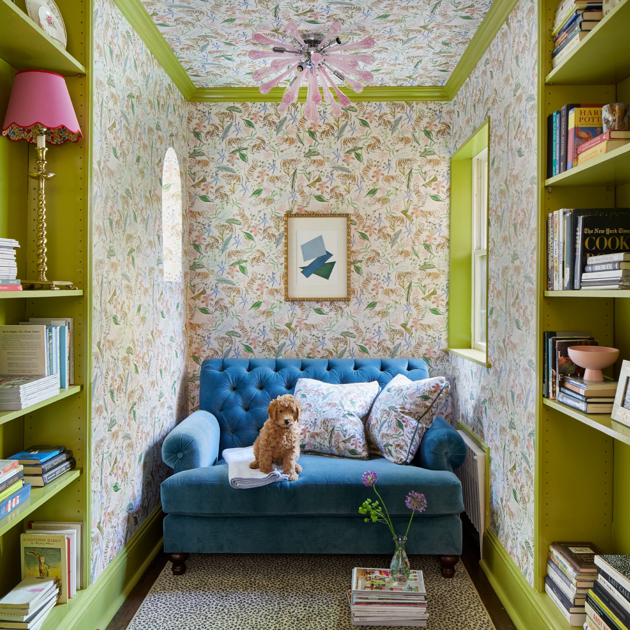 Library corner with books on shelves styled with Pink Chinoiserie Tiger Printed Wallpaper and blue couch with brown dog and Pink Chinoiserie Tiger Printed Pillows on top