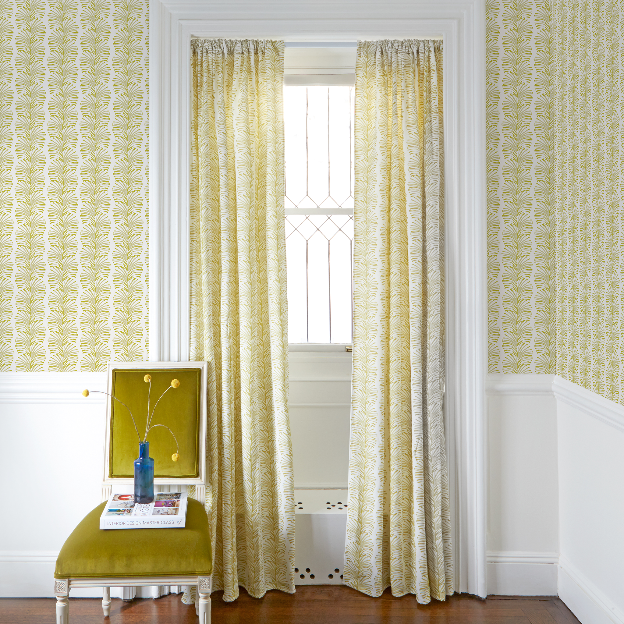 Yellow Stripe Chartreuse Printed Curtains on white rod with Yellow Stripe Chartreuse Printed Wallpaper in front of an illuminated window with Mustard Yellow Velvet chair with plants in blue clear vase on top of white book 