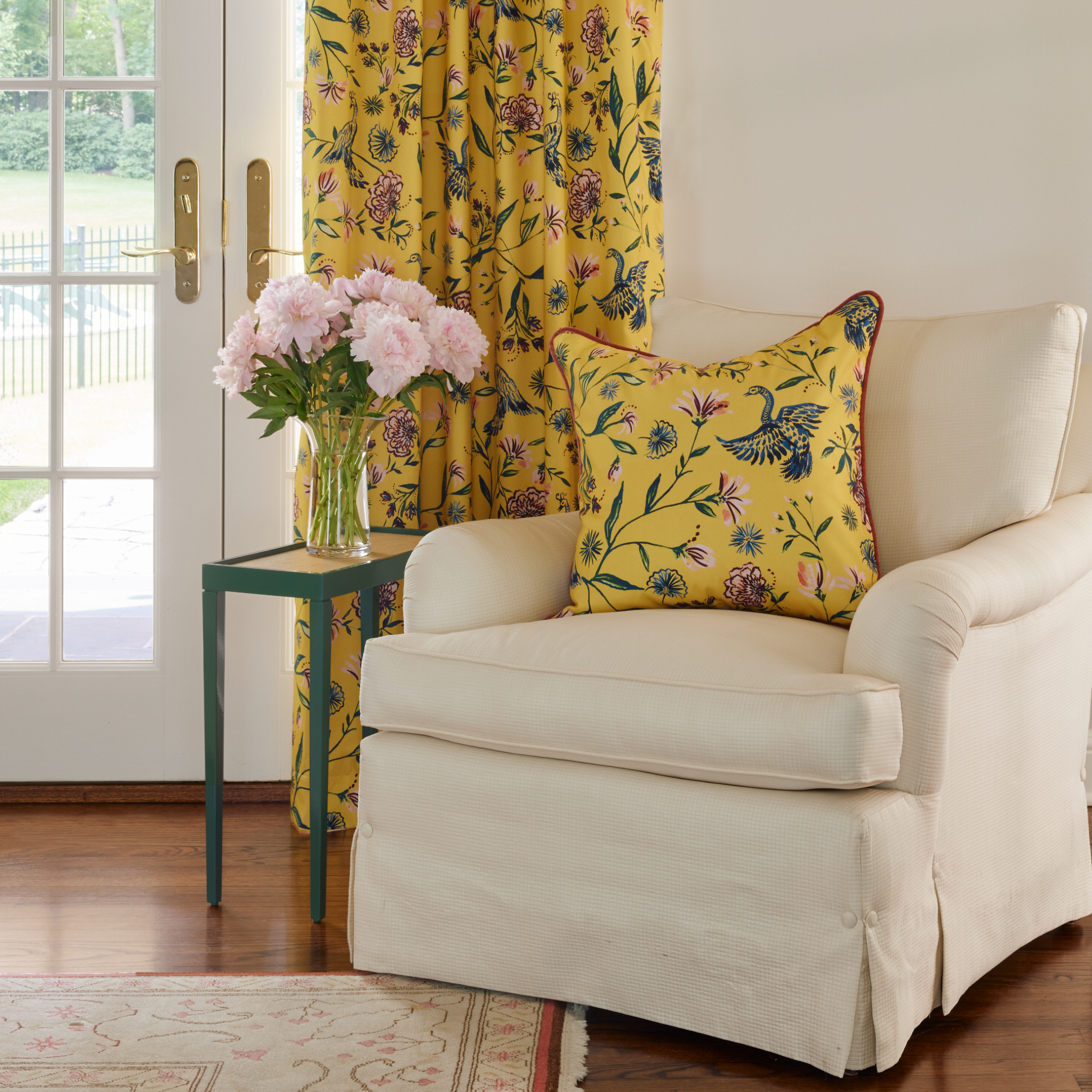 Yellow Chinoiserie printed curtains styled on living room with white arm chair styled with Yellow Chinoiserie printed pillow next to small green table with vase on top full of pink flowers