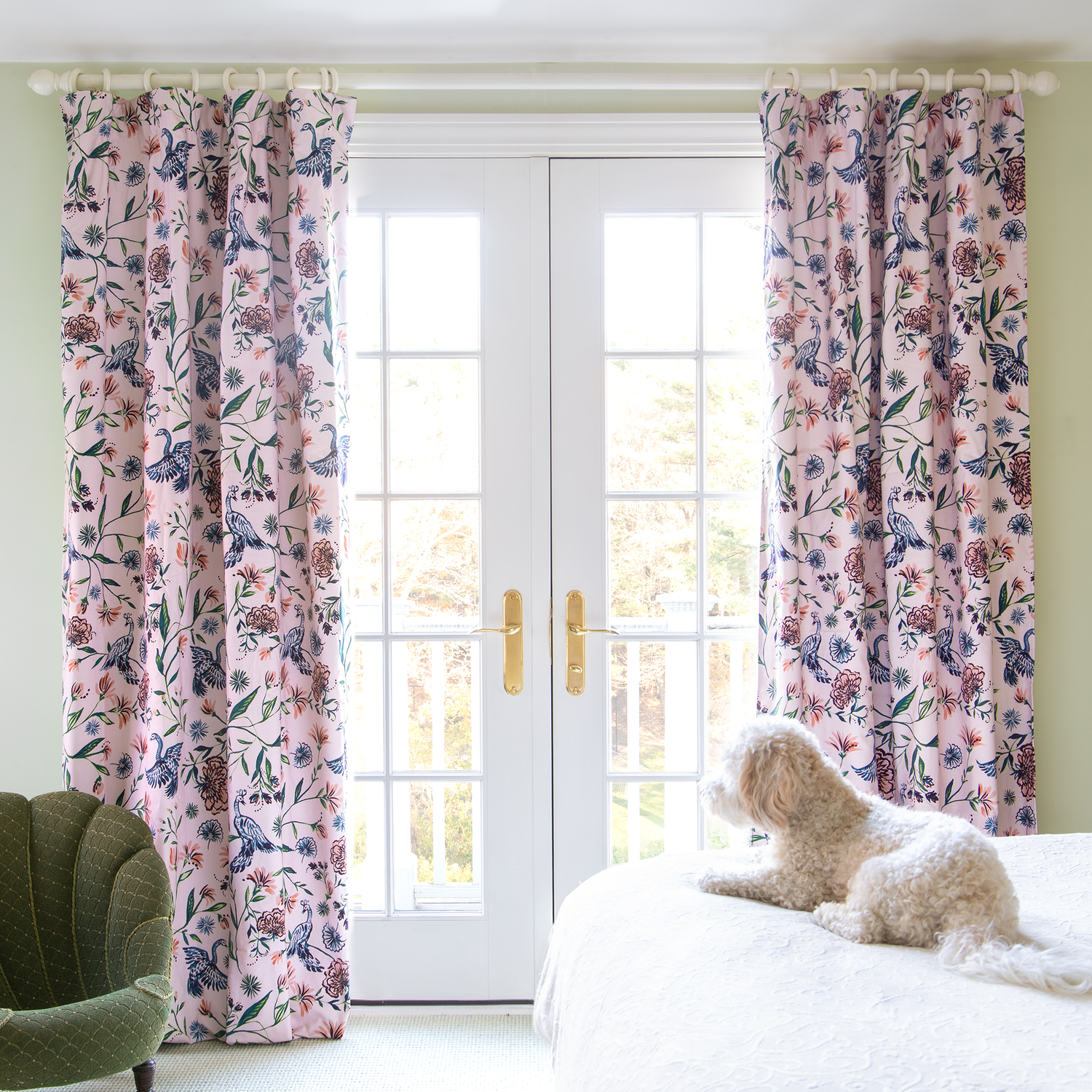 Pink Chinoiserie Printed Curtains hanging from white rod on window in front of dog in white bed and fern velvet sofa chair to the left