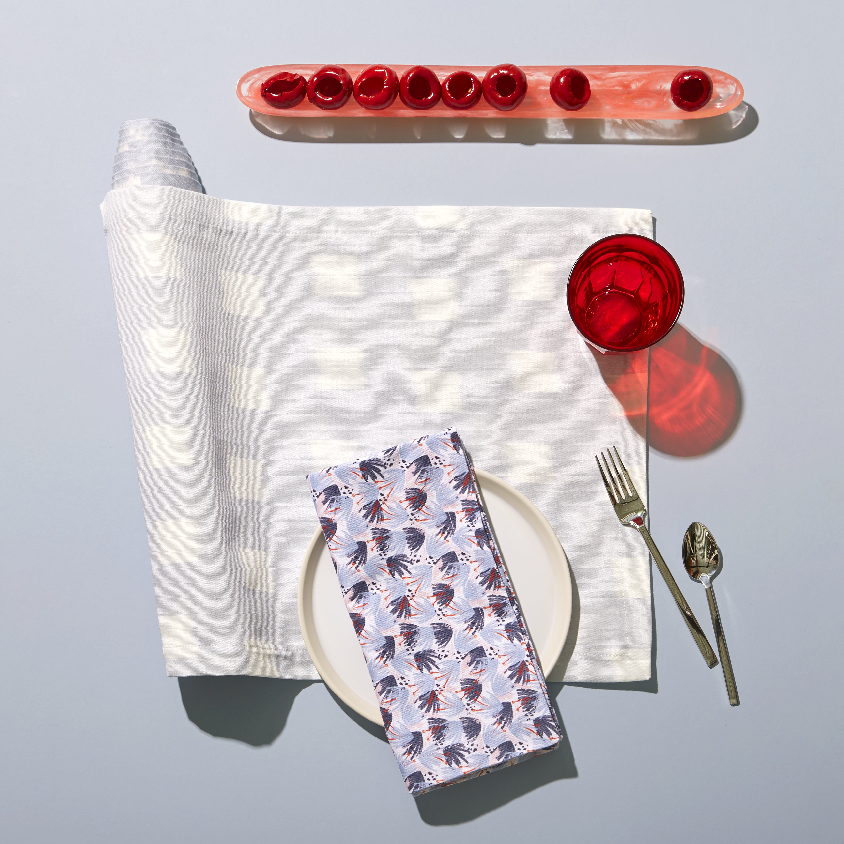 Red and Blue  Printed Napkin on top of white plate next to silverware and red glass over Sky Blue Pattern Printed Runner