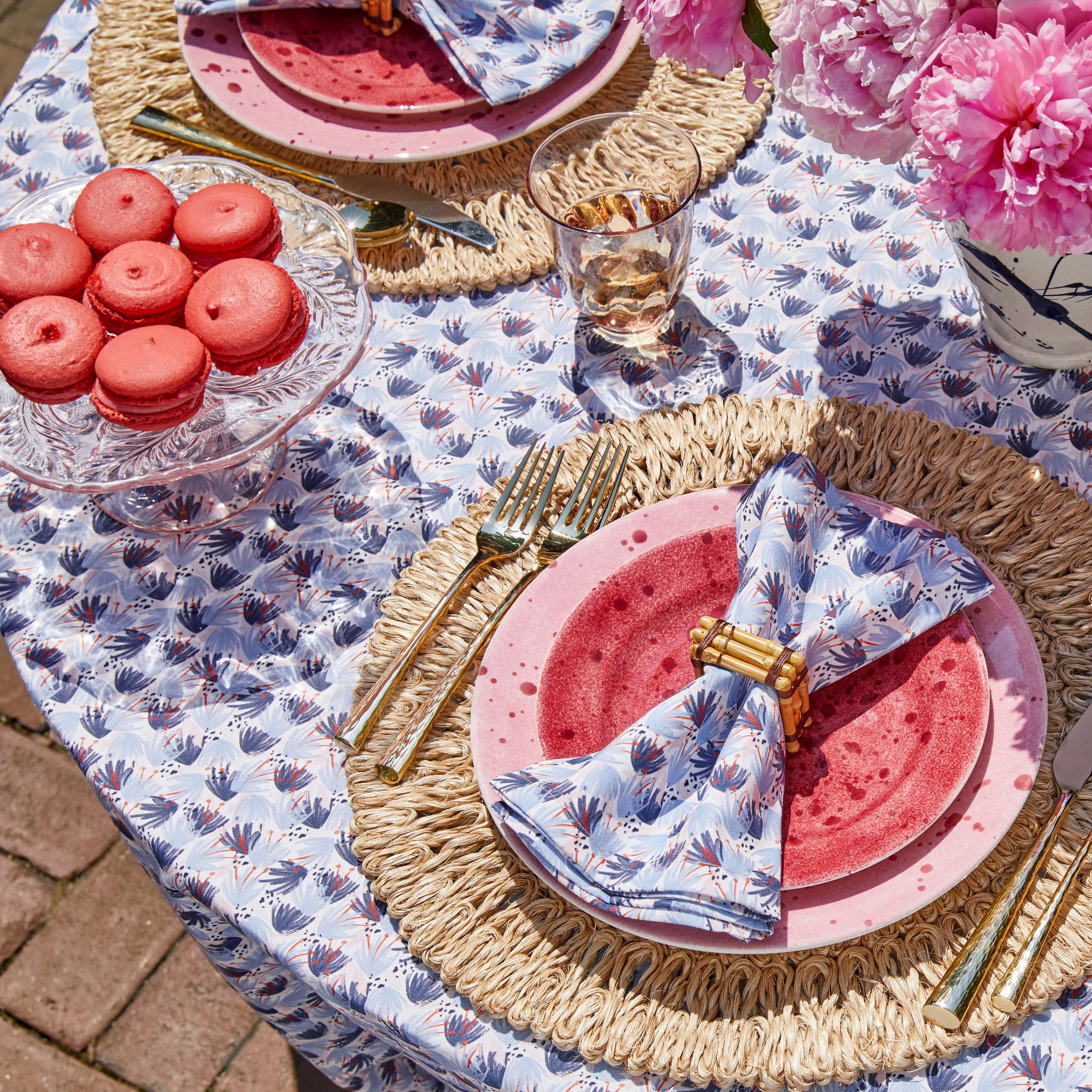 Sky Blue Pattern Printed Tablecloth styled with gold silverware and red and blue printed napkins on top of red and pink plates by seven red macaroons on clear plate