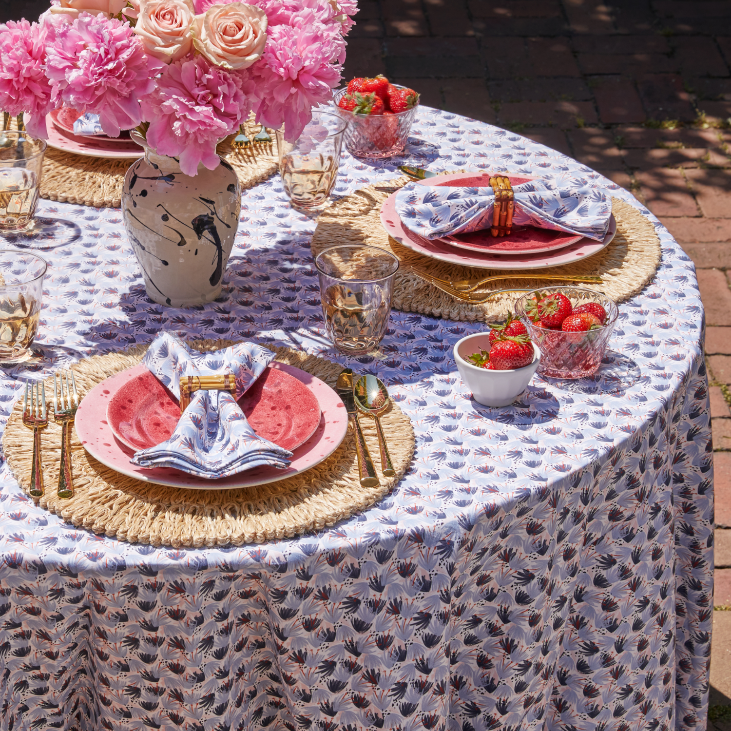 Sky Blue Pattern Printed Tablecloth styled with gold silverware and red and blue printed napkins on top of red and pink plates around the table surrounding pink flowers in cream vase