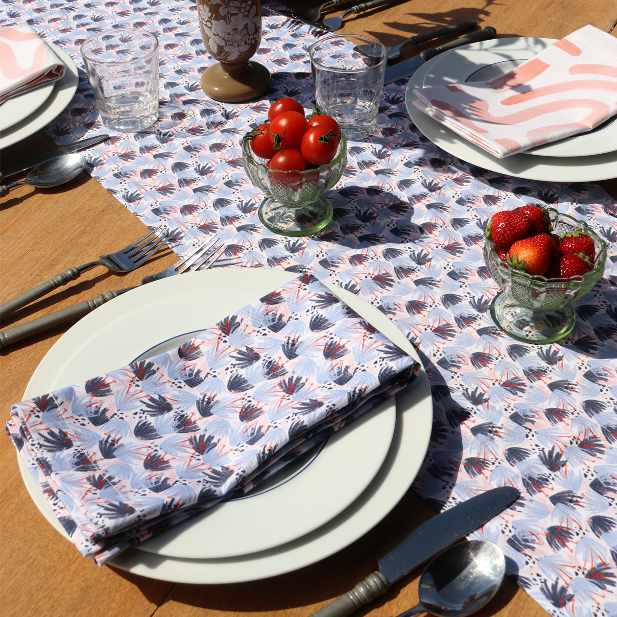 Red and Blue Printed runner close-up with red and blue printed napkin on top of two white plates by silverware in front of cup of strawberries and cup of cherry tomatoes 