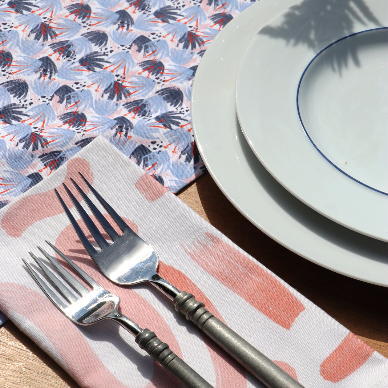 Pink Graphic Printed Napkin Close-up under silverware next to two white plates and Red and Blue Printed Runner