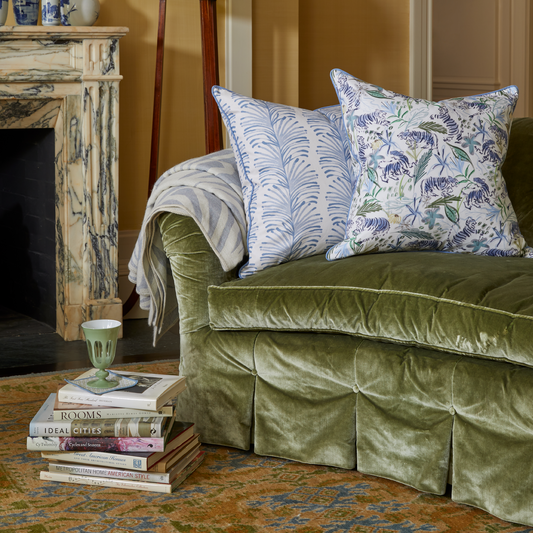 Couch Close-Up styled with Sky Blue Botanical Stripe Pillow and Green Tiger Printed Pillow with books stacked on rug with green glass on top