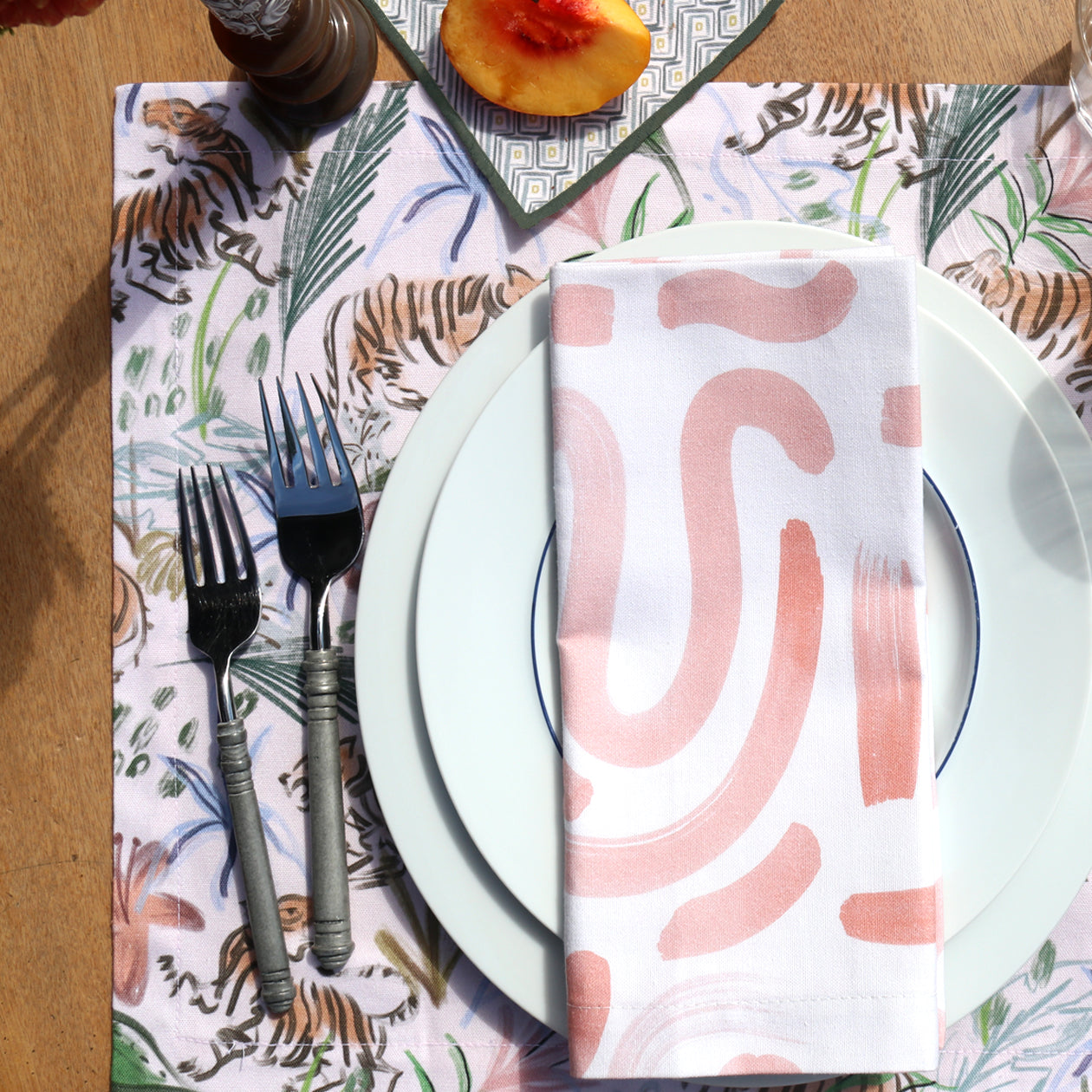 Close-up of table setting styled with Pink Chinoiserie Tiger Printed Placemat under two white plates with Pink Graphic Printed Napkin on top by silverware 