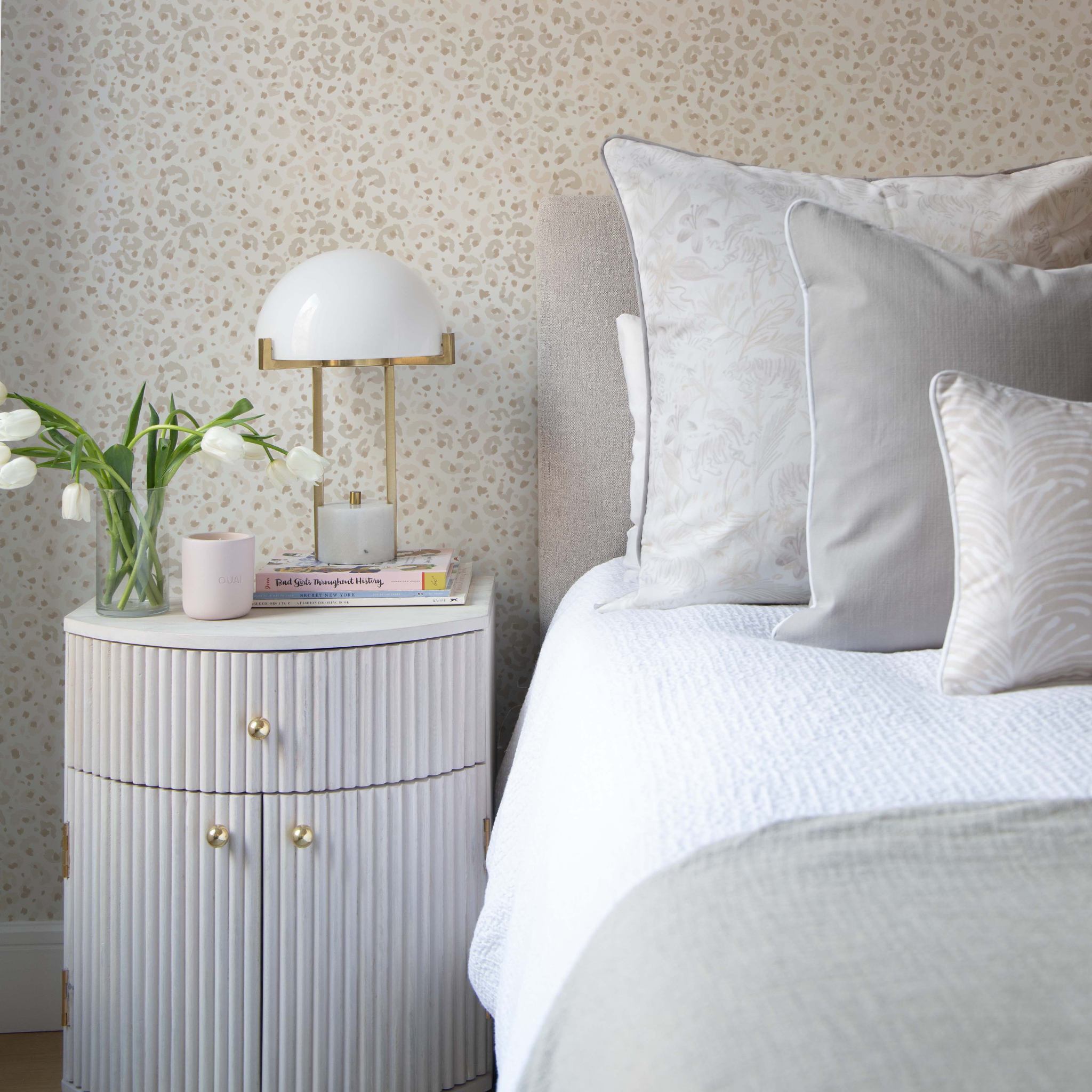 Bedroom corner styled with Beige Animal Print Wallpaper and Beige Chinoiserie Tiger Printed pillow, Linen Oat Pillow, and Beige Botanical Stripe Printed Lumbar next to white nightstand with white flowers and white lamp on top