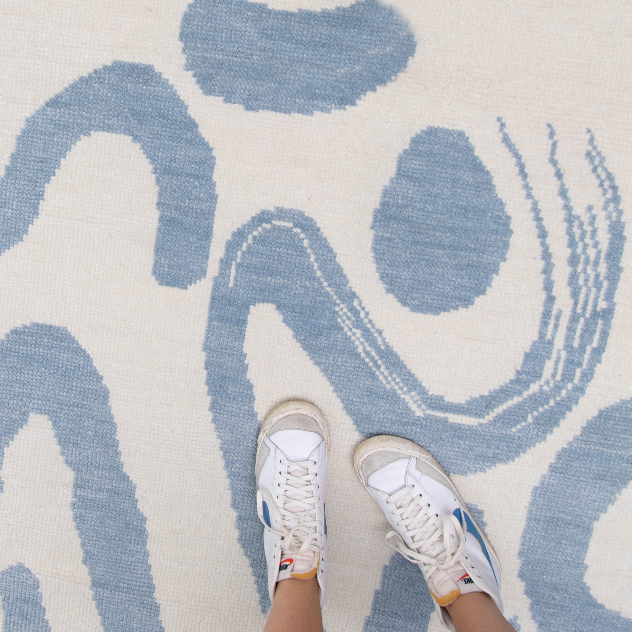 Sky Blue Printed Rug Close-up with white tennis shoes on woman's feet in the bottom right corner