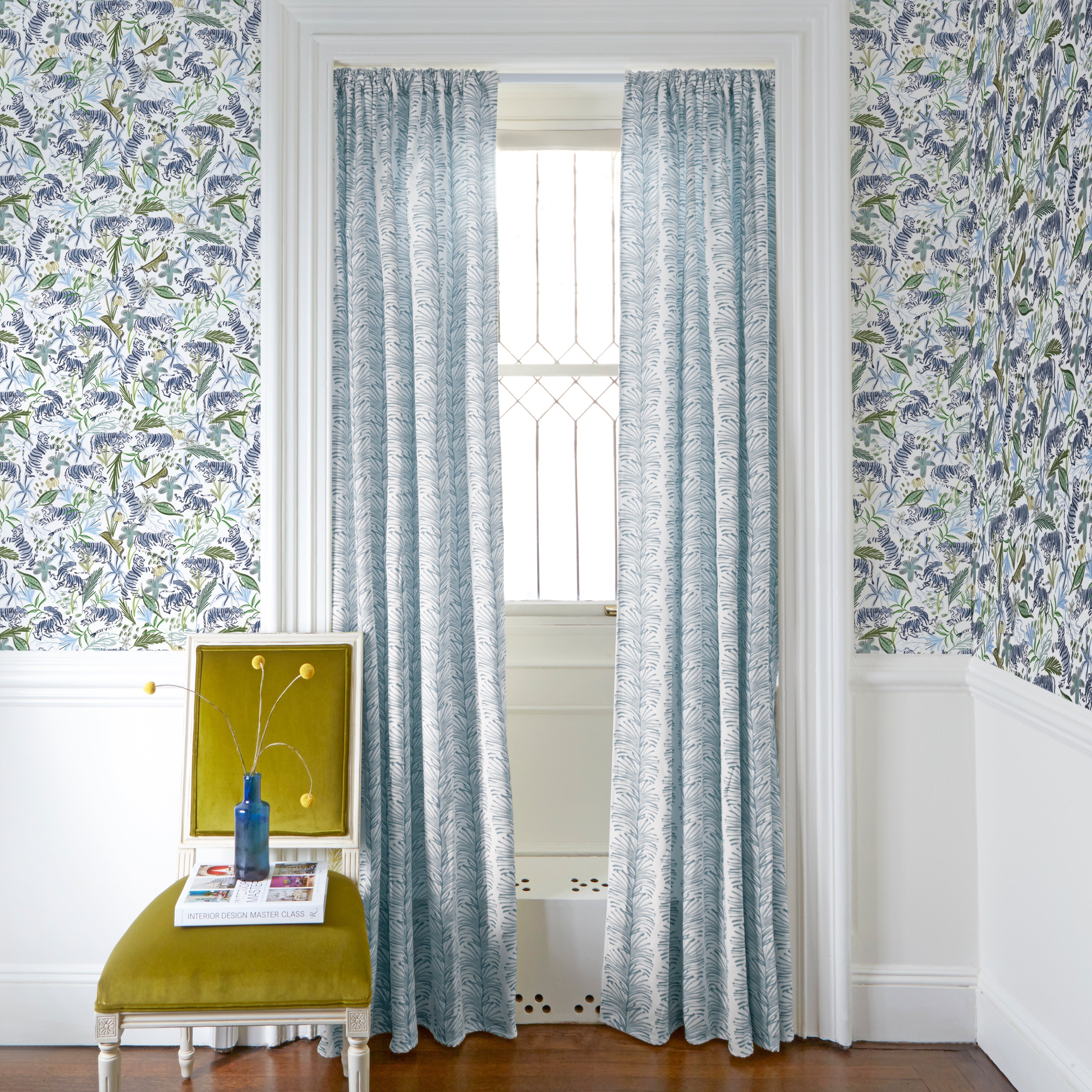 Sky Blue Botanical Stripe Printed Curtains on white rod in front of an illuminated window with Green Tiger Printed Wallpaper by Mustard Yellow Velvet chair with plants in blue clear vase on top of white book
