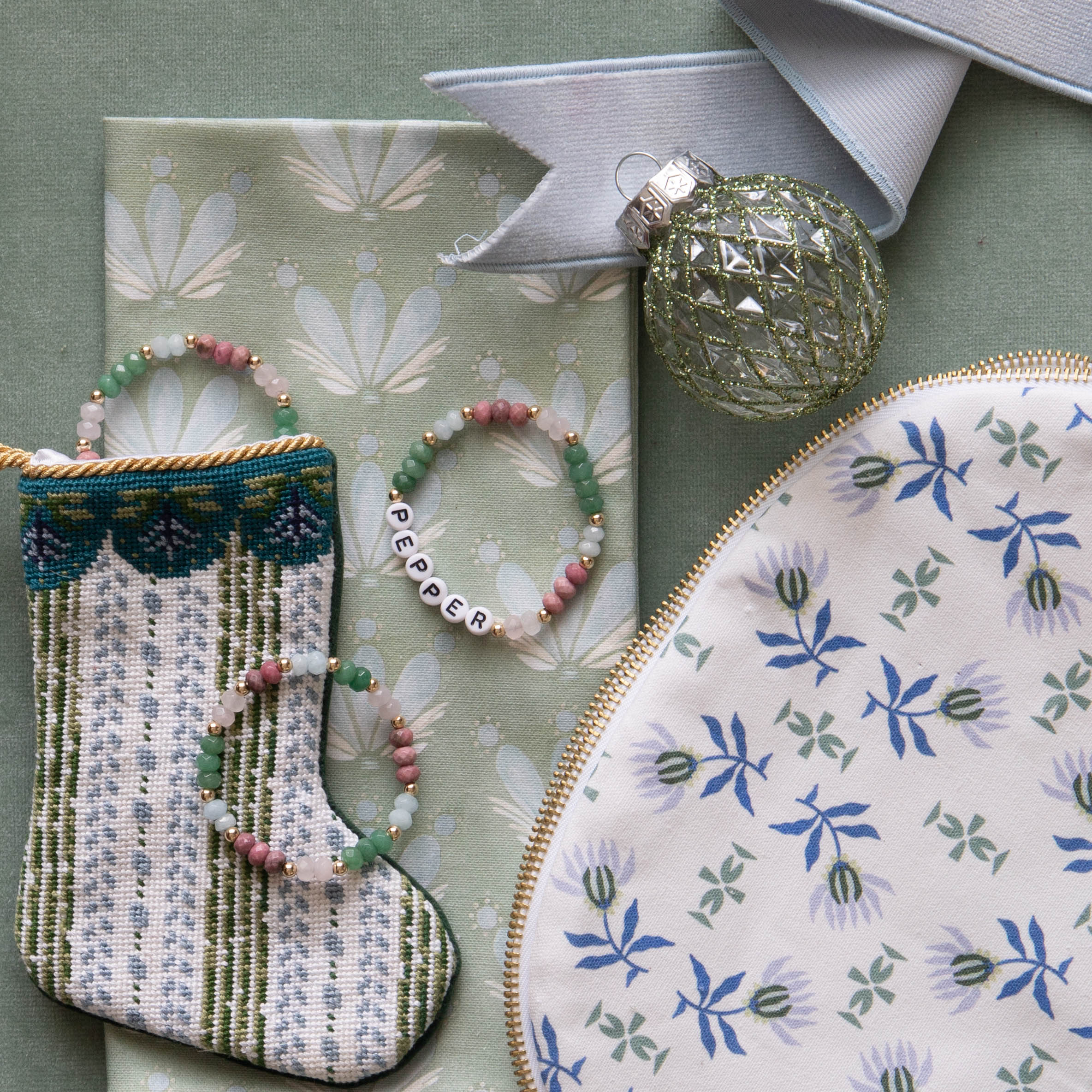 Blue & Green Striped Hand Sown Mini Bauble Stocking on Coastal Inspired Green and Blue Printed Swatch next to Blue & Green Floral Printed Pouch and three beaded bracelets by Christmas ornament 
