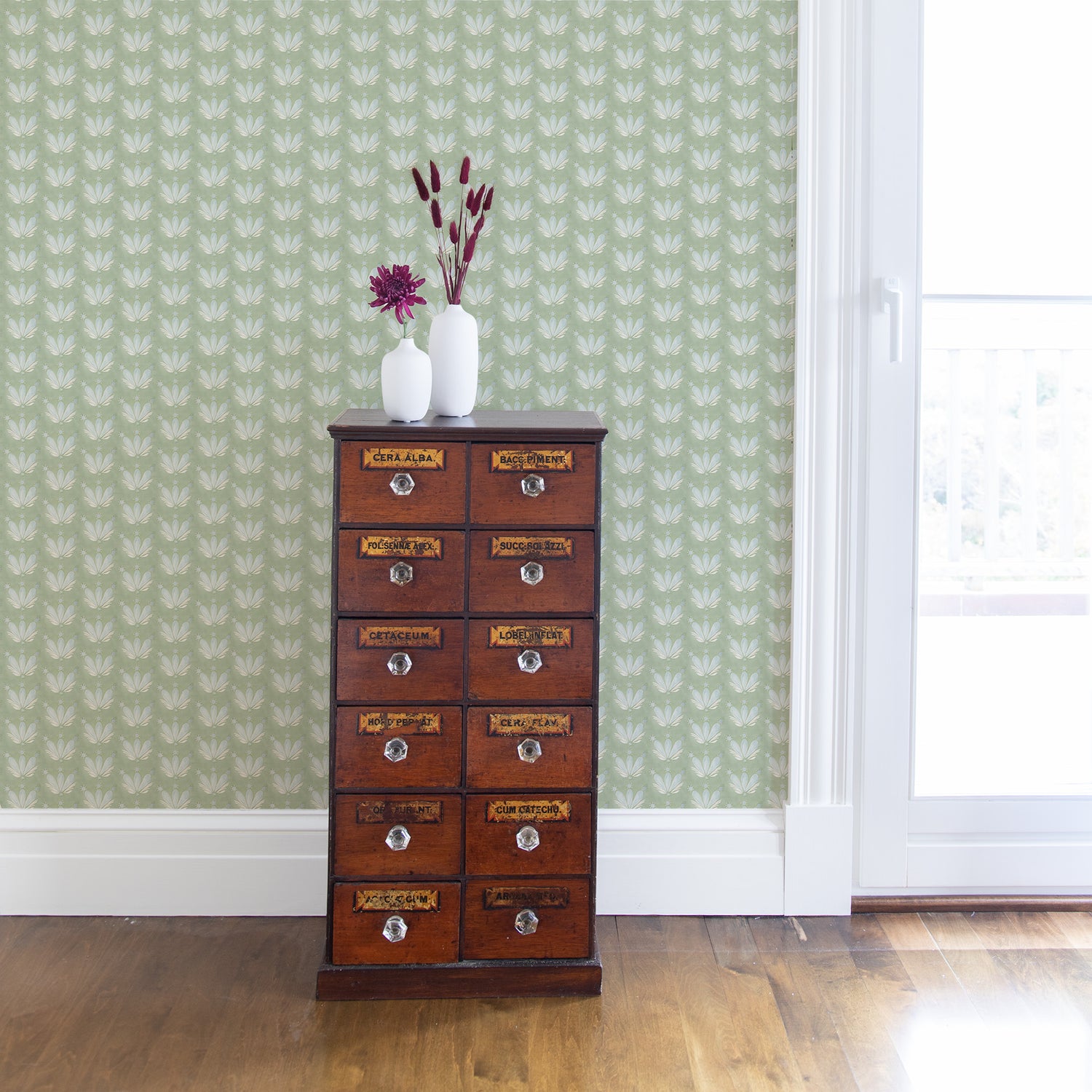 Corner with wooden cabinet styled with two white vases with pink flowers on top and a Blue & Green Floral Drop Repeat Printed Wallpaper next to illuminated window