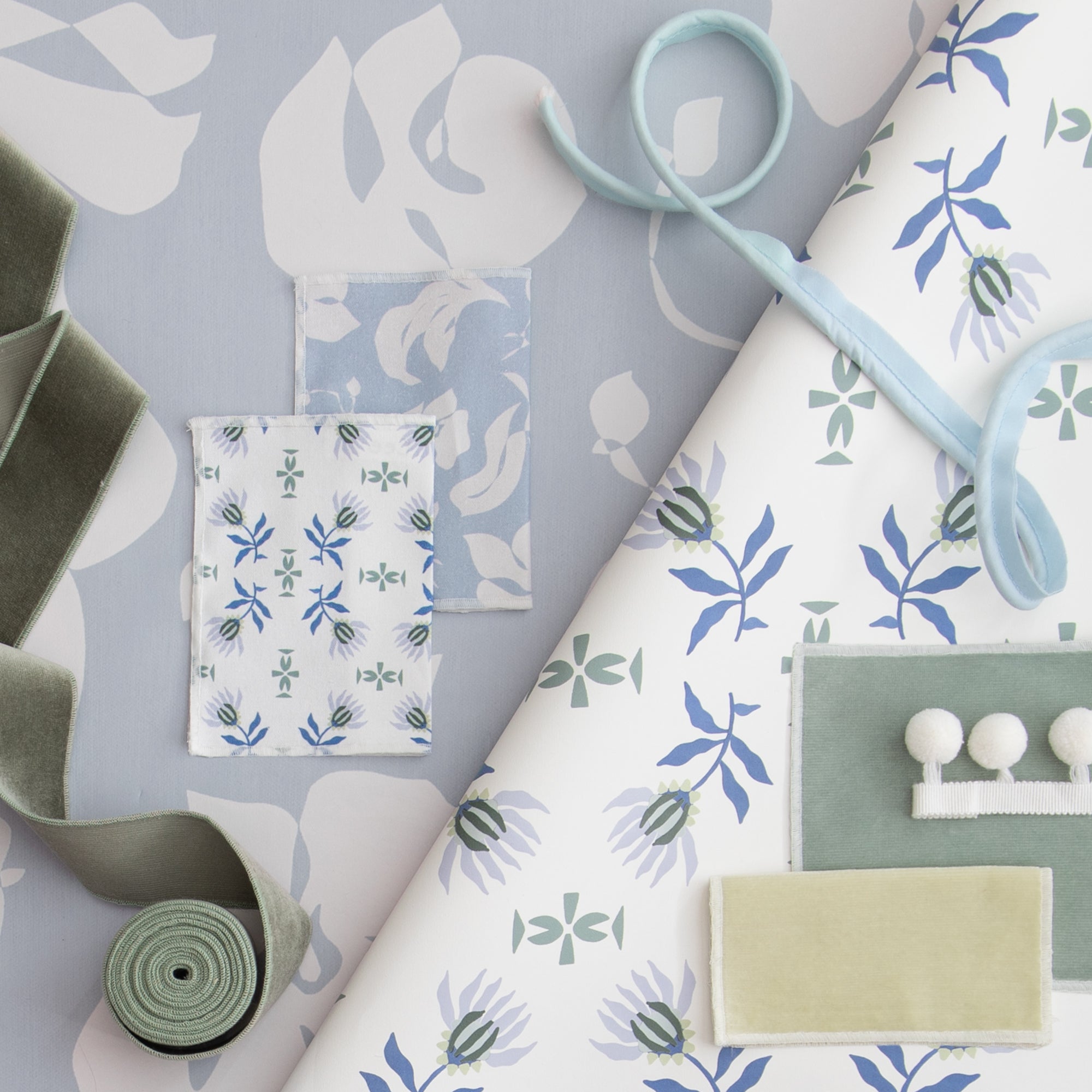 interior design moodboard with blue and green floral wallpaper and fabric swatches, blue piping, white pom poms, and fern green velvet band trim