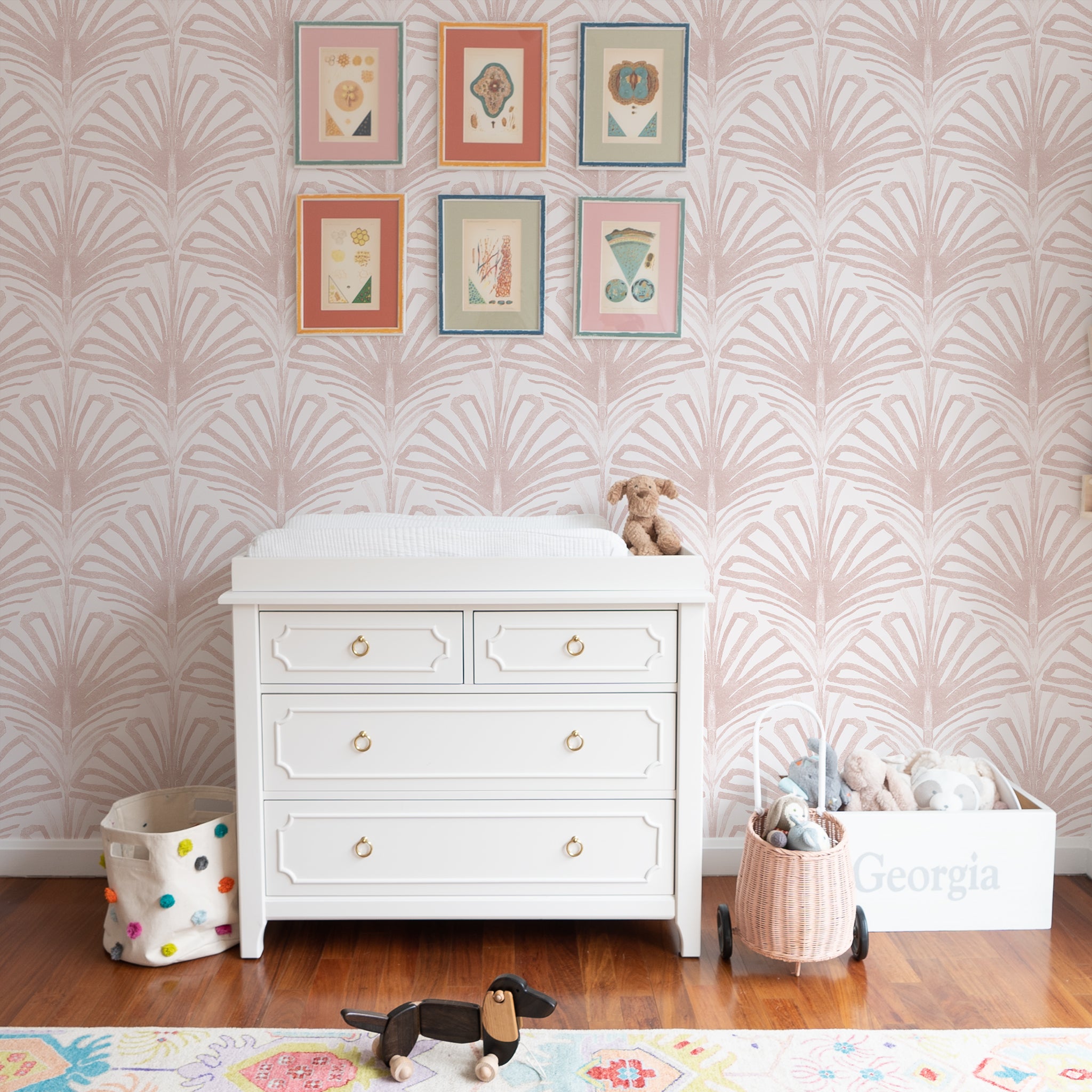 White Changing Table Close-up styled with rose pink palm printed wallpaper and six framed artworks hung on wall
