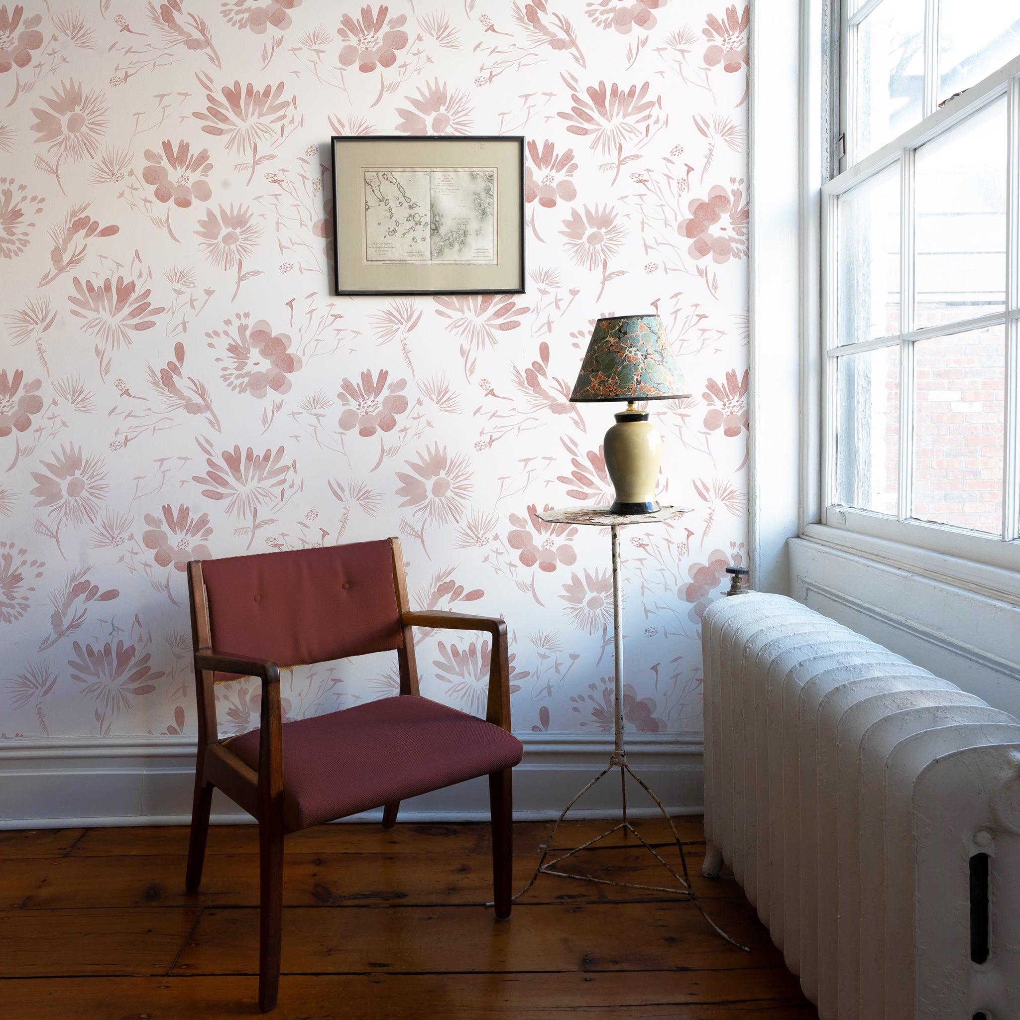 Nursery Room corner styled with Pink Floral custom wallpaper with wooden red chair in front by green and floral lamp on white circular small table next to window