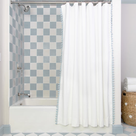 White Cotton shower curtain hanging on rod in front of white tub in bathroom with blue and white tiles