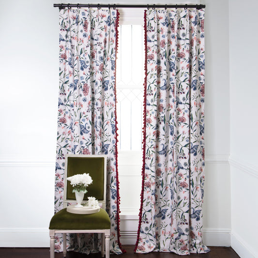Cream Chinoiserie Printed curtains with Cherry fringe on metal rod in front of an illuminated window with Green Moss chair with white flowers in white vase on top of plate