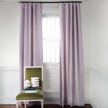 Lilac Velvet Curtains on metal rod in front of an illuminated window with a Moss Green Velvet chair with two empty white vases on top of stacked books