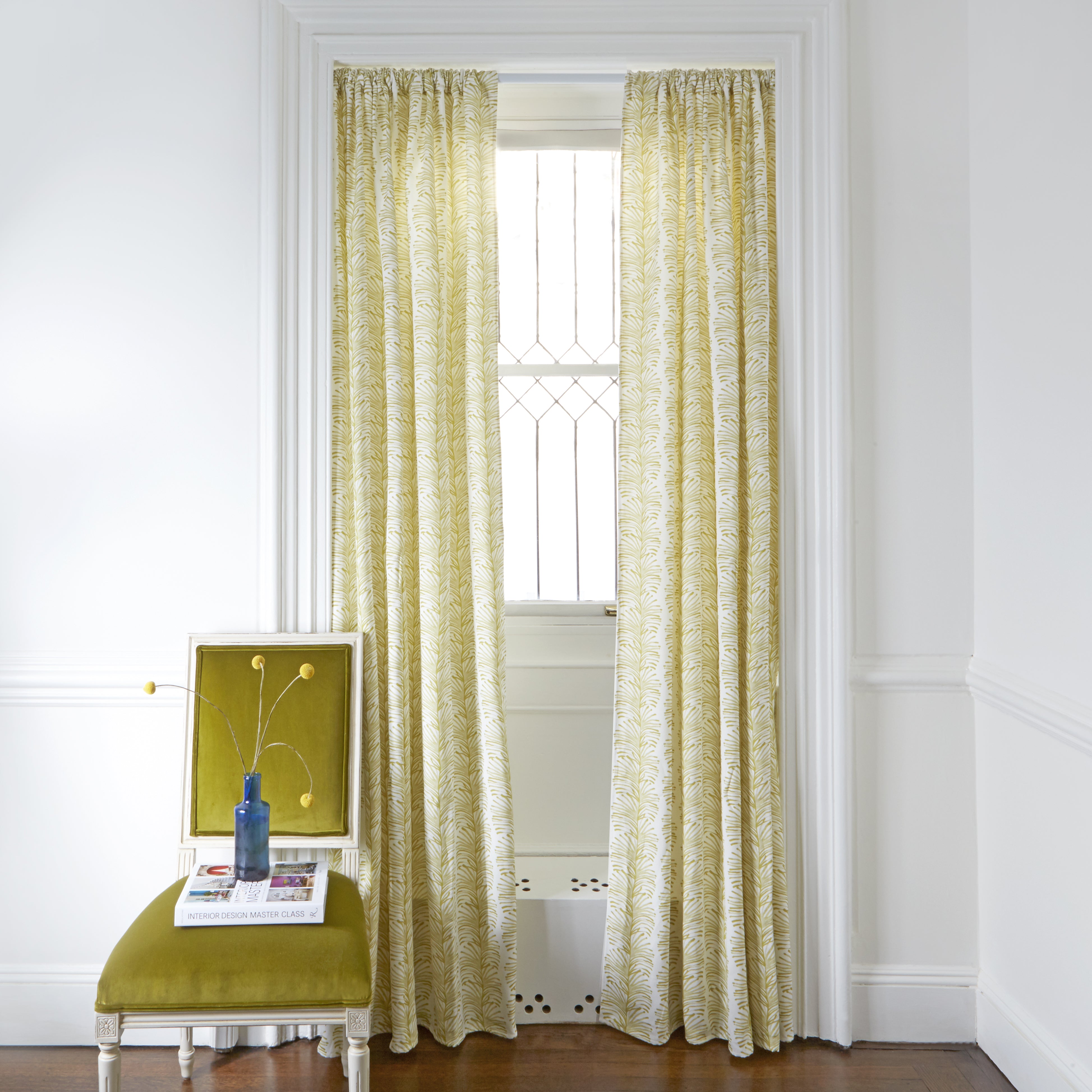 Yellow Stripe Chartreuse Printed Curtains on white rod in front of an illuminated window with Mustard Yellow Velvet chair with plants in blue clear vase on top of white book