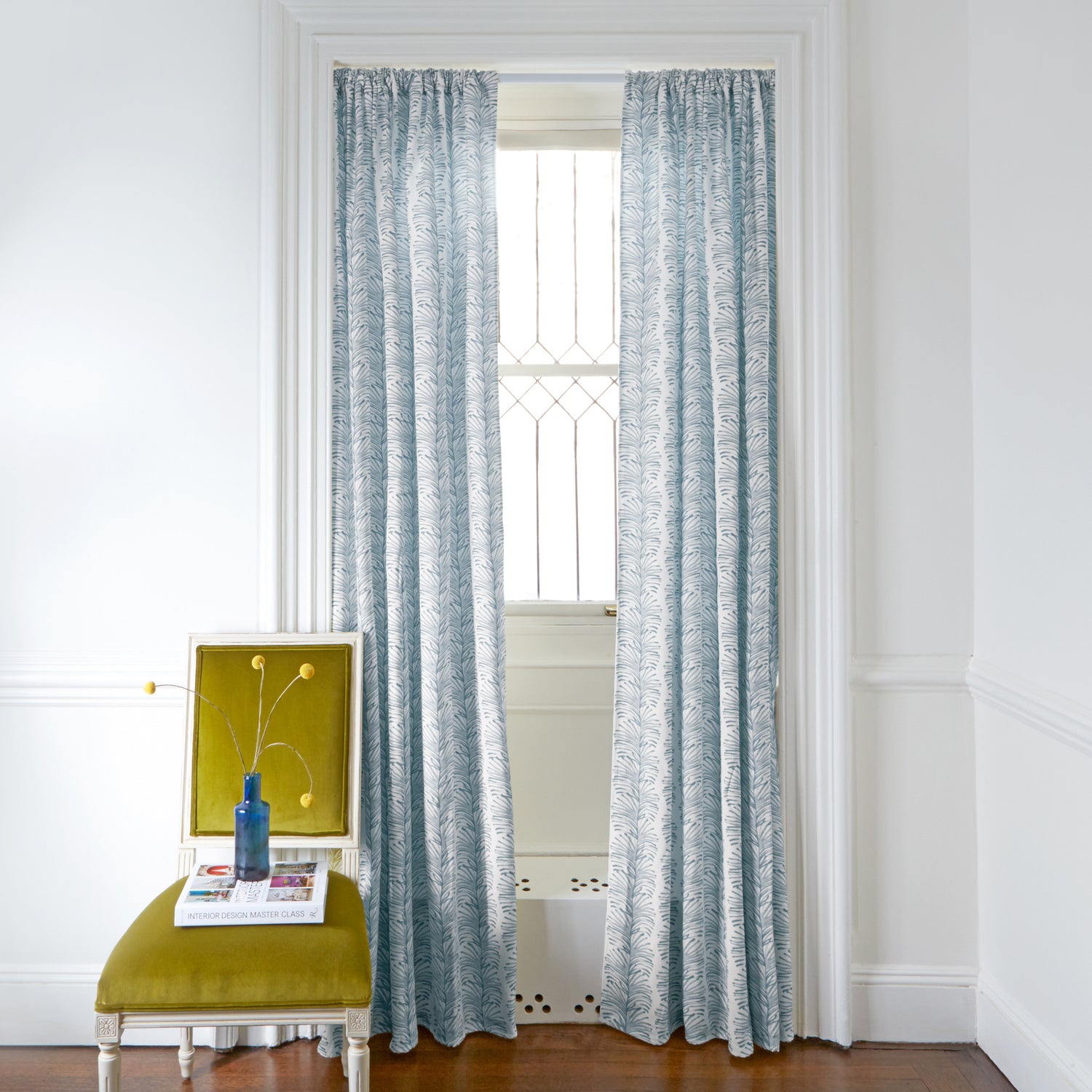 Sky Blue Botanical Stripe Printed Curtains on white rod in front of an illuminated window with Mustard Yellow Velvet chair with plants in blue clear vase on top of white book