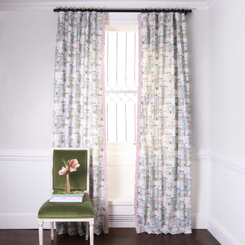 Hand-painted Floral Printed Curtains with Pink Band on metal rod in front of an illuminated window with Green Velvet chair with Pink flowers in golden vase on top of stacked books