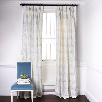 Blue & Green Striped Printed Curtains on metal rod in front of an illuminated window with Sky Blue Velvet chair with grapes in bowl on top of stacked books