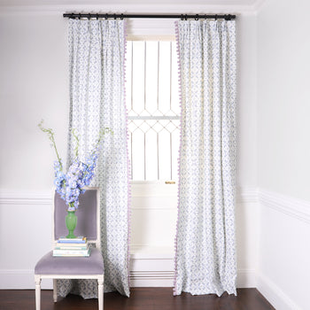 Blue & Green Floral Printed Curtains on metal rod in front of an illuminated window with Lavender Velvet chair with purple flowers in green vase on stacked books