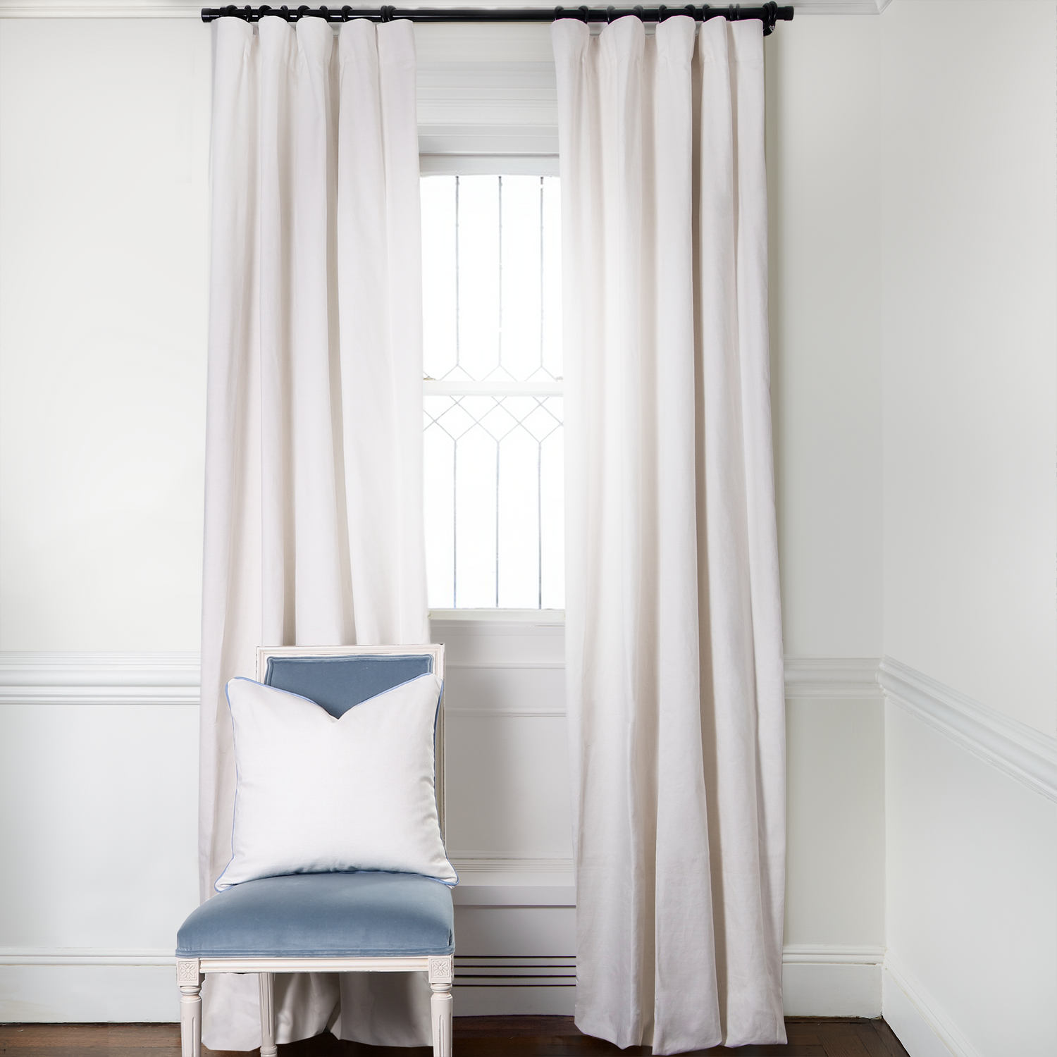 Natural White Linen Curtains on metal rod in front of an illuminated window with Baby Blue Velvet chair with Natural White Pillow on it