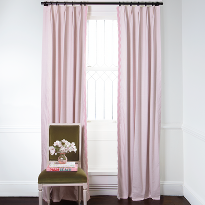 Pink Geometric Printed Curtains on metal rod in front of an illuminated window with Green Velvet chair with pink and white flowers in clear pink vase on top of stacked books