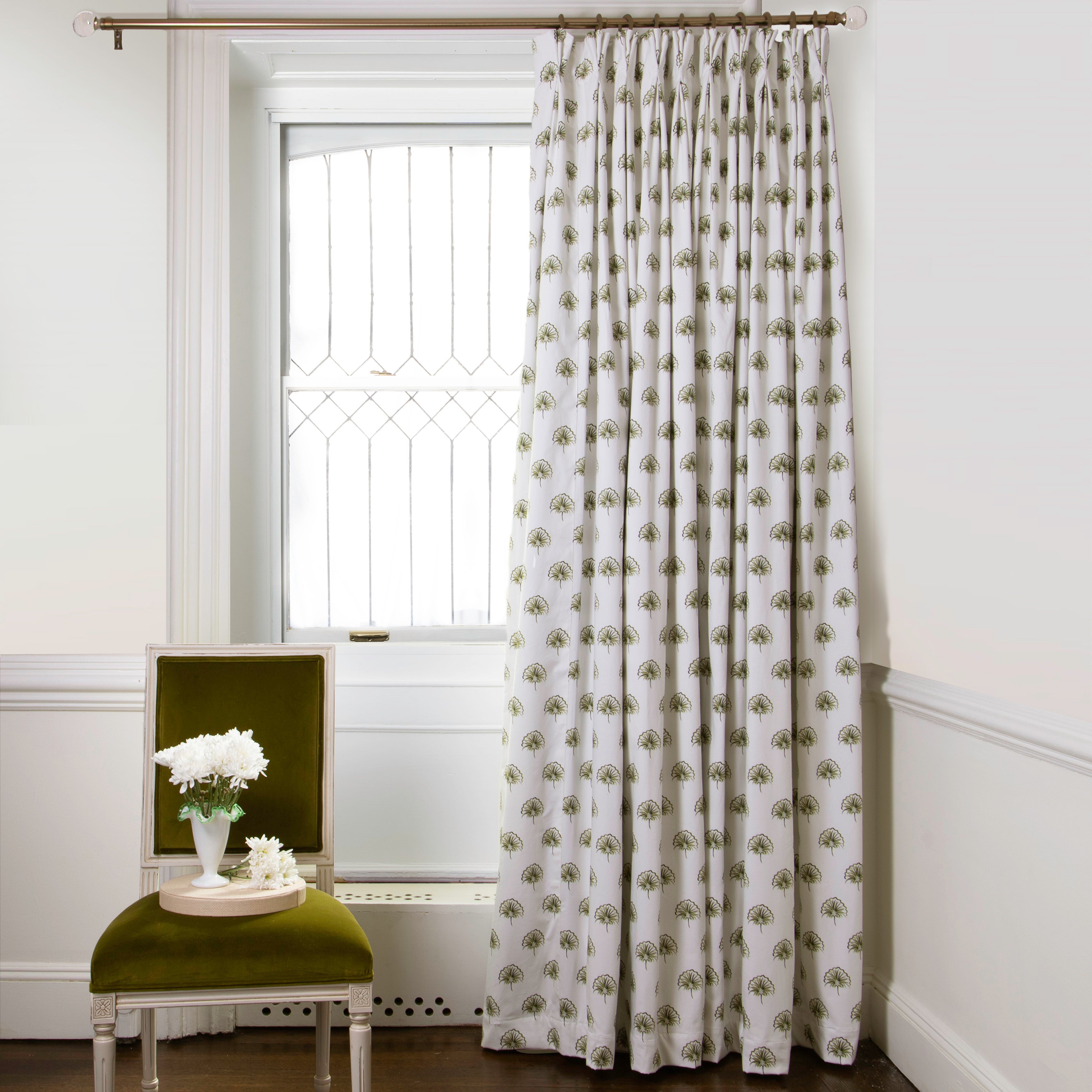 Green Floral Printed curtains on metal rod in front of an illuminated window with Green Moss chair with white flowers in white vase on top of plate