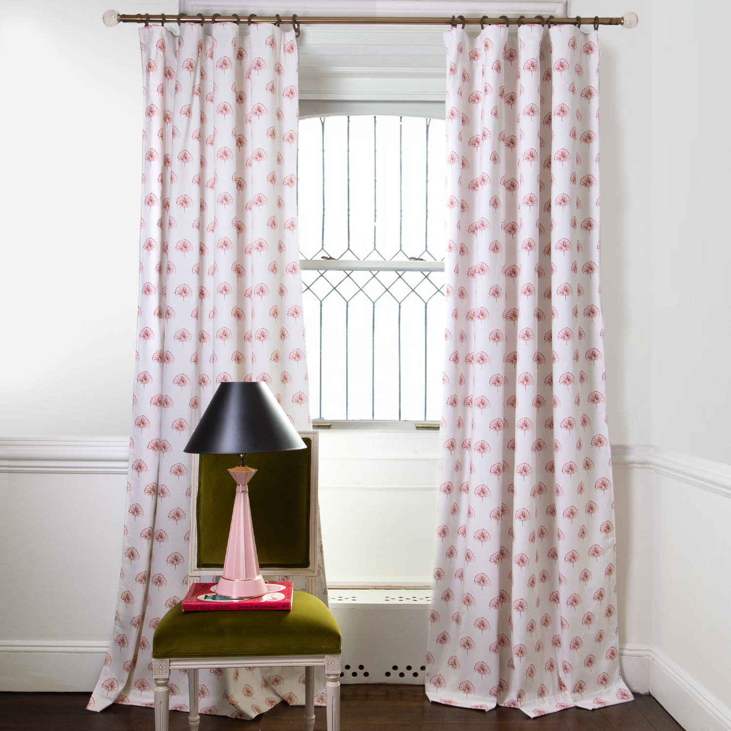 Rose Floral Printed curtains on metal rod in front of an illuminated window with Green Moss chair with pink and black lamp on top of book