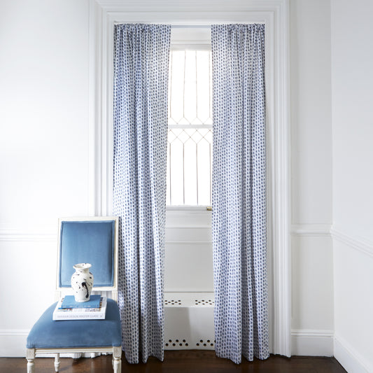 Sky and Navy Blue Poppy Printed Curtains on metal rod in front of an illuminated window with Sky Blue Velvet chair with white and black vase on top of stacked books