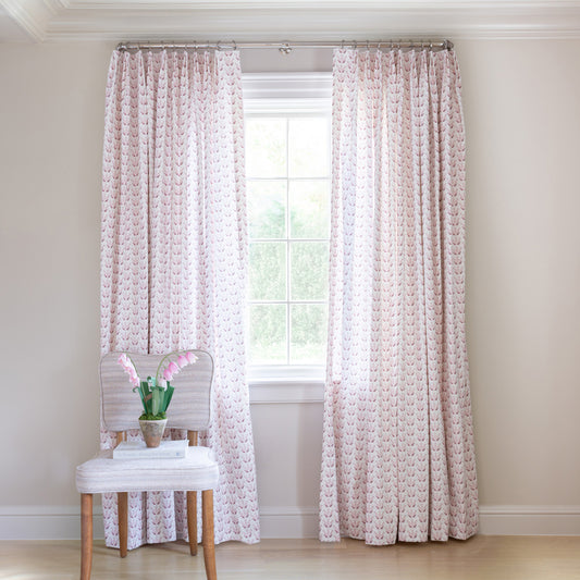 Pink & Burgundy Drop Repeat Floral Printed Curtains on black rod in front of an illuminated window with a burgundy Velvet chair with plants in clear pitcher vase on top of stacked books