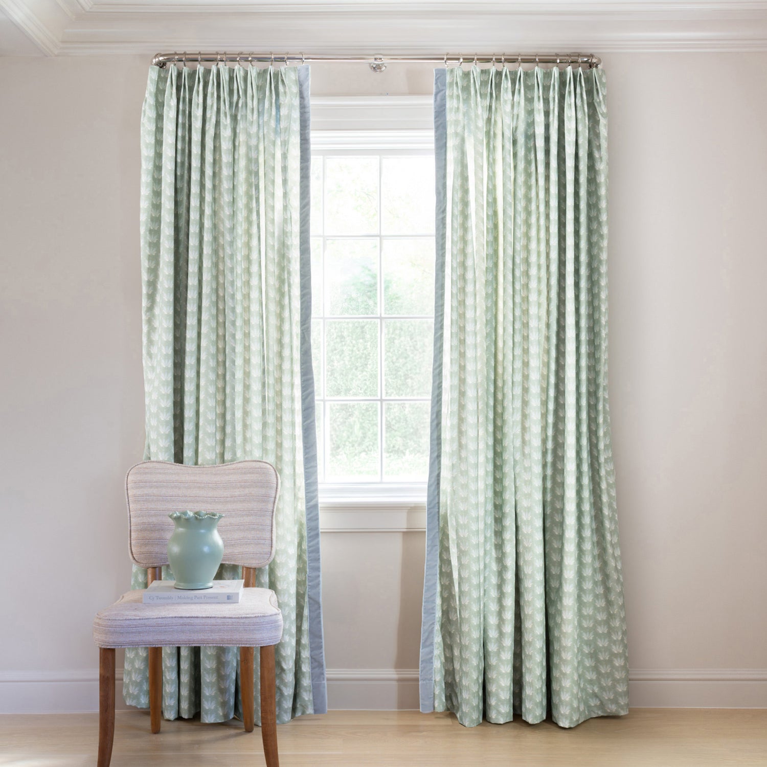 Blue & Green Floral Drop Repeat Printed Curtains on black rod in front of an illuminated window with a Blue Green Velvet chair with blue flowers in blue sculpted vase on top of stacked books