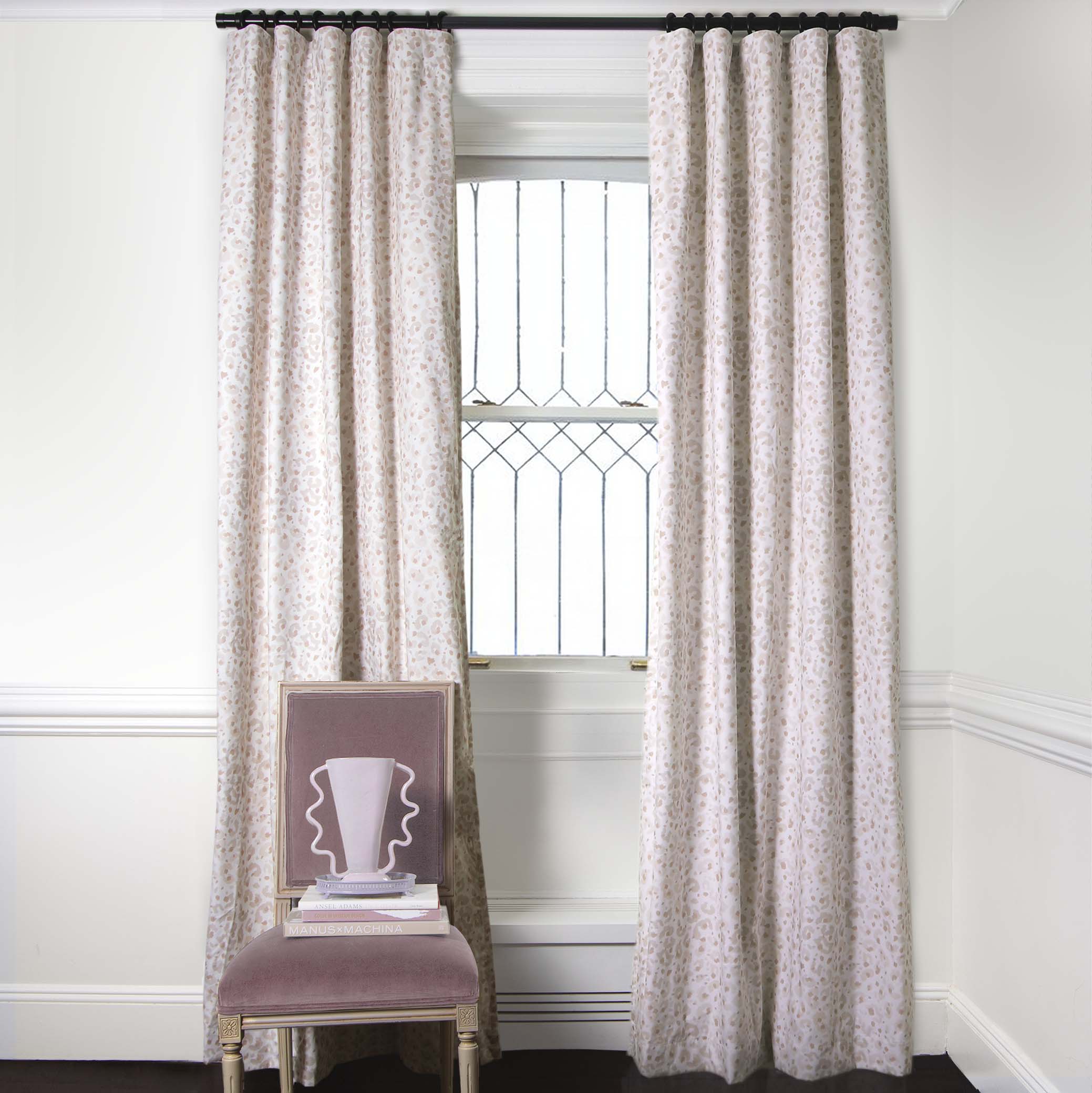 Beige Animal Print Curtains on metal rod in front of an illuminated window with Pink Velvet chair with pink vase on top of stacked books