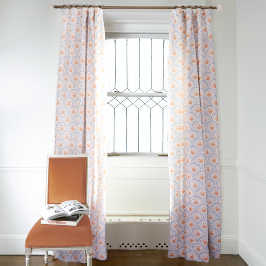 Art Deco Palm Pattern Printed Curtains on metal rod in front of an illuminated window with Orange Velvet chair with books on top