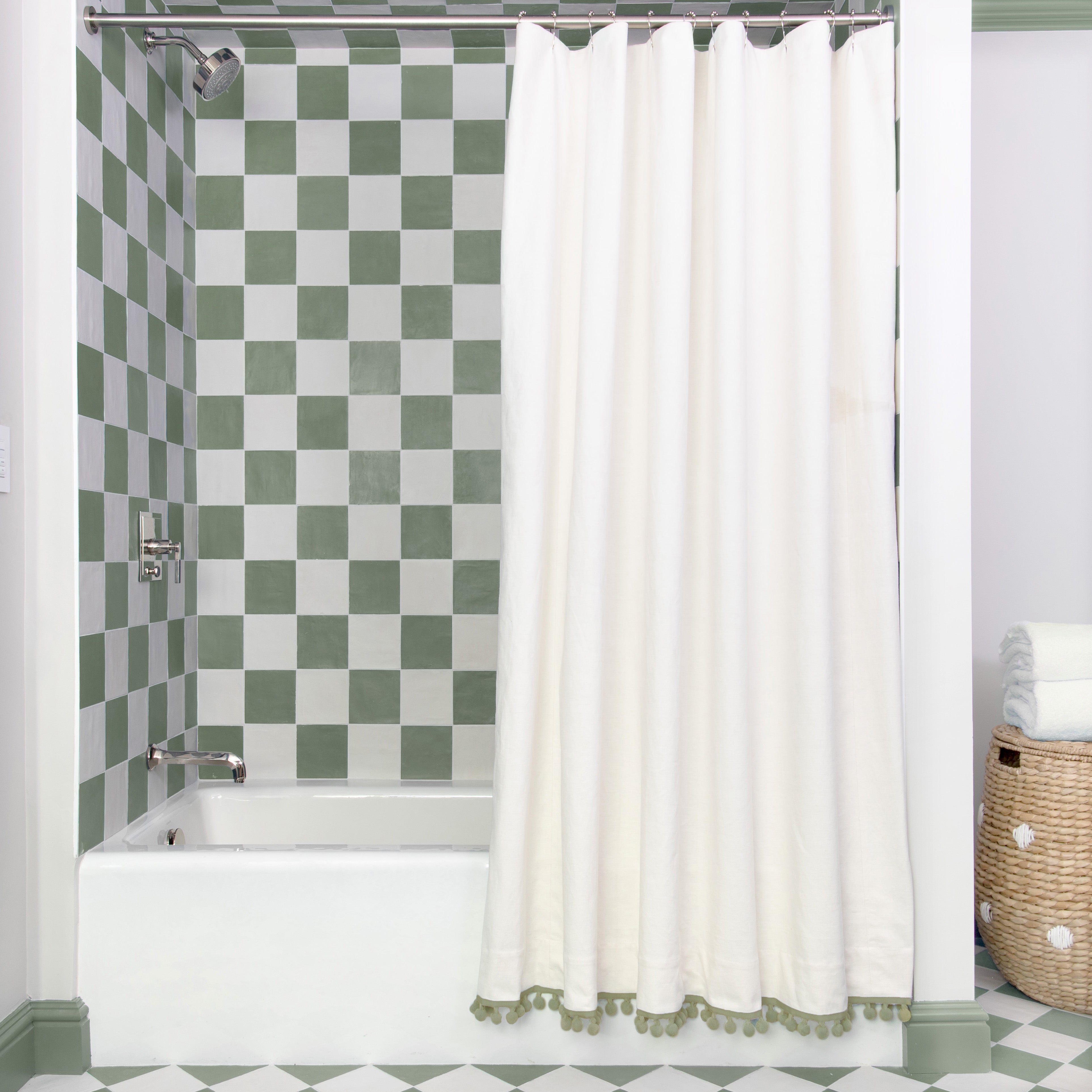 Natural White shower curtain hanging on rod in front of white tub in bathroom with green and white tiles