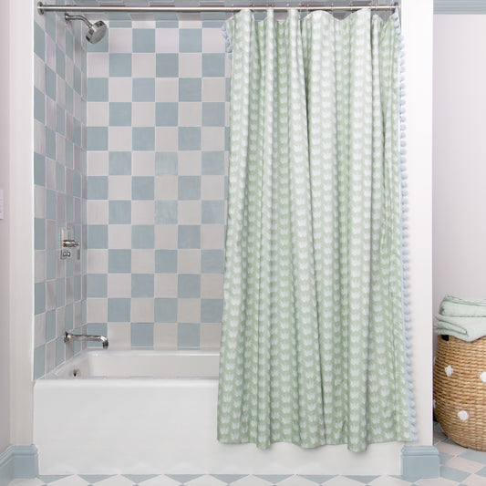 Coastal Inspired Green and Blue Printed shower curtain hanging on rod in front of white tub in bathroom with blue and white tiles