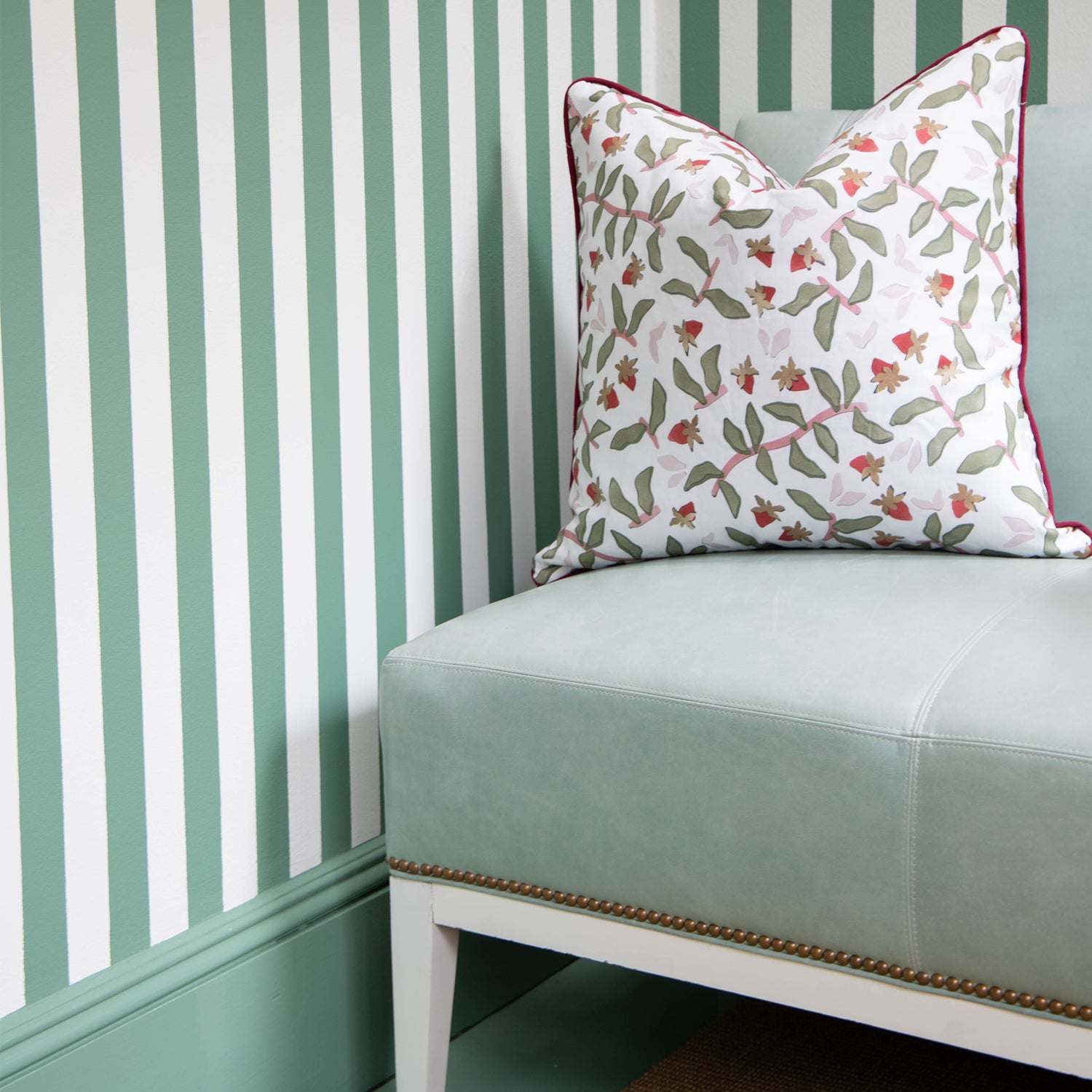 Corner with green and white striped wallpaper styled with a Strawberry & Botanical Printed Pillow on Green Leather Couch