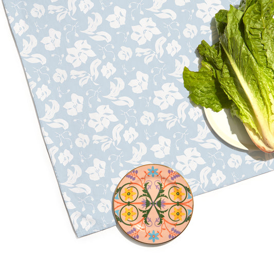 Corner Close-Up of Cornflower Blue Floral Printed Tablecloth with a colorful geometric shape printed plate and a white plate with lettuce on top